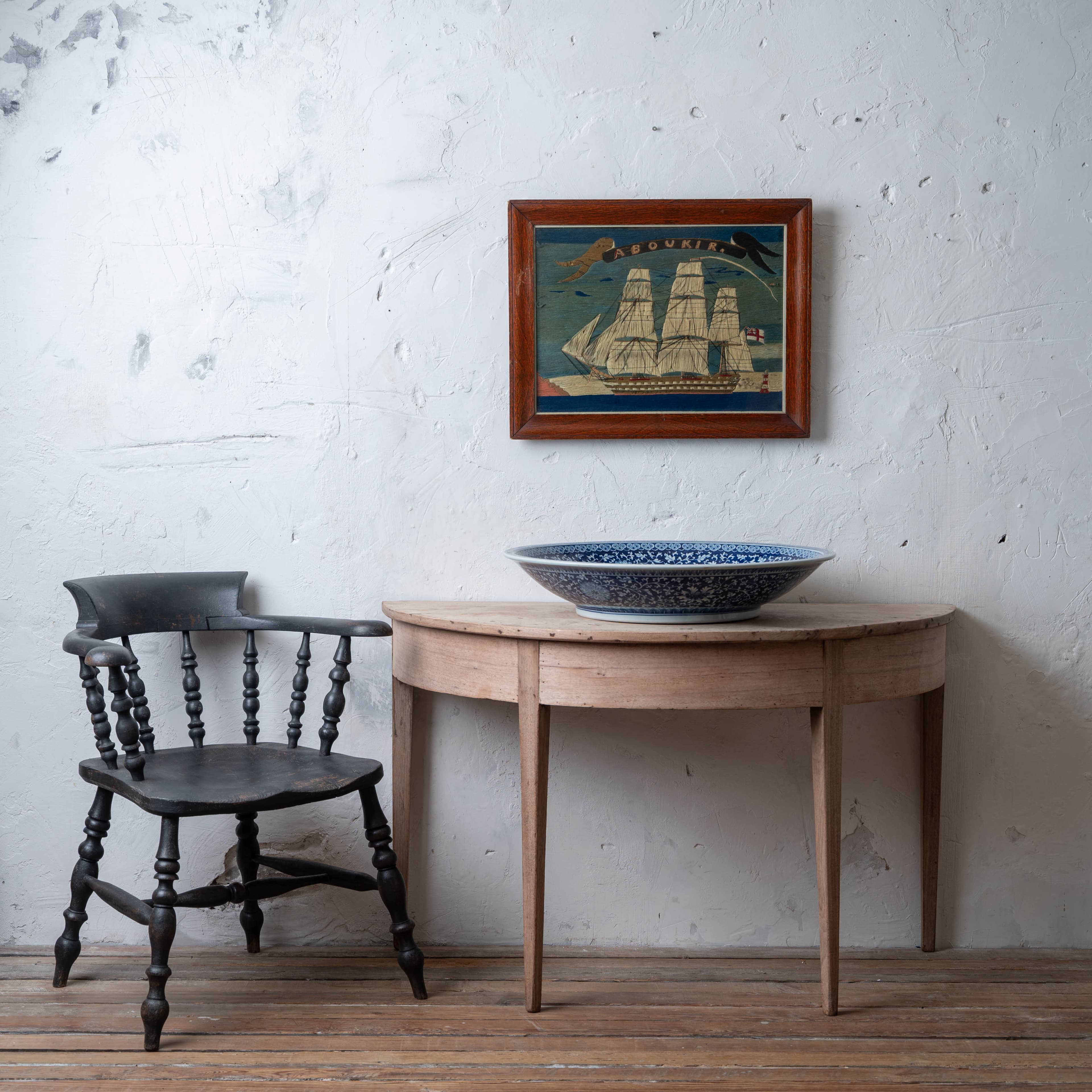 The H.M.S. Aboukir sailor's woolwork hung above a demilune table, with the captain's chair in black